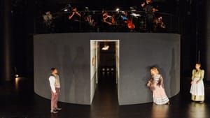 The orchestra atop a circular gray structure about 10 feet tall, with the cast members performing in front of it.