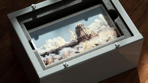 Seen in a small gray box that perfectly fits a stack of photos, an ambiguous photo of an explosion, with clouds of smoke.