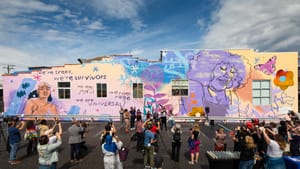 A wide shot of the mural with an audience in front of it, with a few people near a podium.