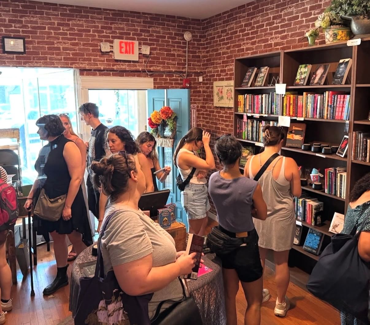 About a dozen people browse books inside a small city bookstore with brick walls and full shelves.