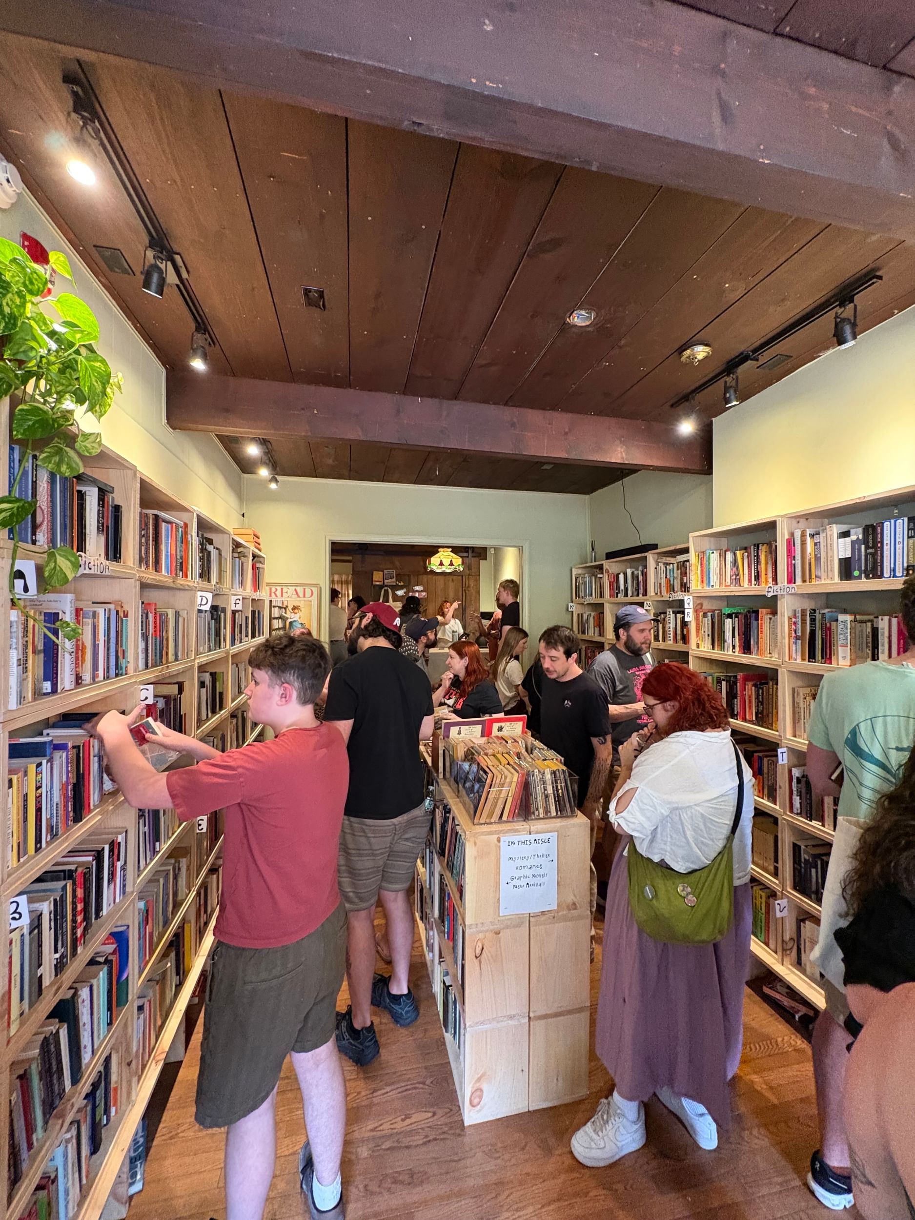 A crowd of book shoppers in a small city store with high shelves and heavy brown wooden beams above.