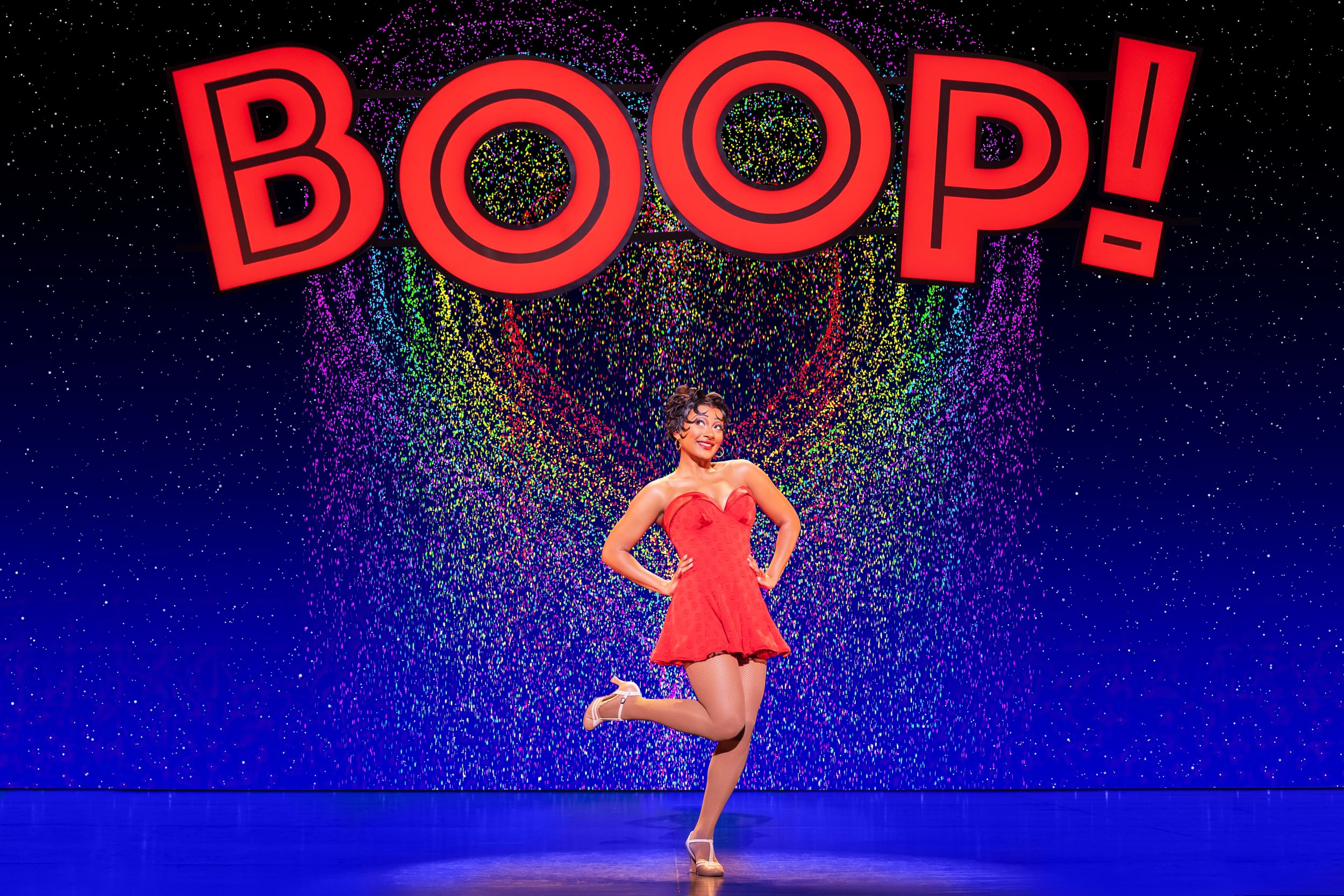 A woman in a sparkling red mini dress and black hair stands center stage, beneath large letters that spell out BOOP!.