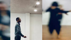 An image of a man in casual clothes in a rehearsal space. It's imposed over another image, it's blurry w/ dancers rehearsing