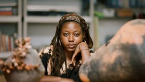 Portrait of Gbadebo, materials in front are out of focus, she’s in the middle looking to camera, resting her head on her hand