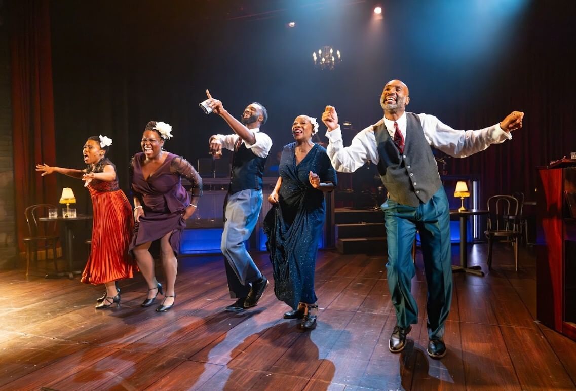 The five actors, in colorful evening wear, dance exuberantly in a line on a stage dressed like a speakeasy.