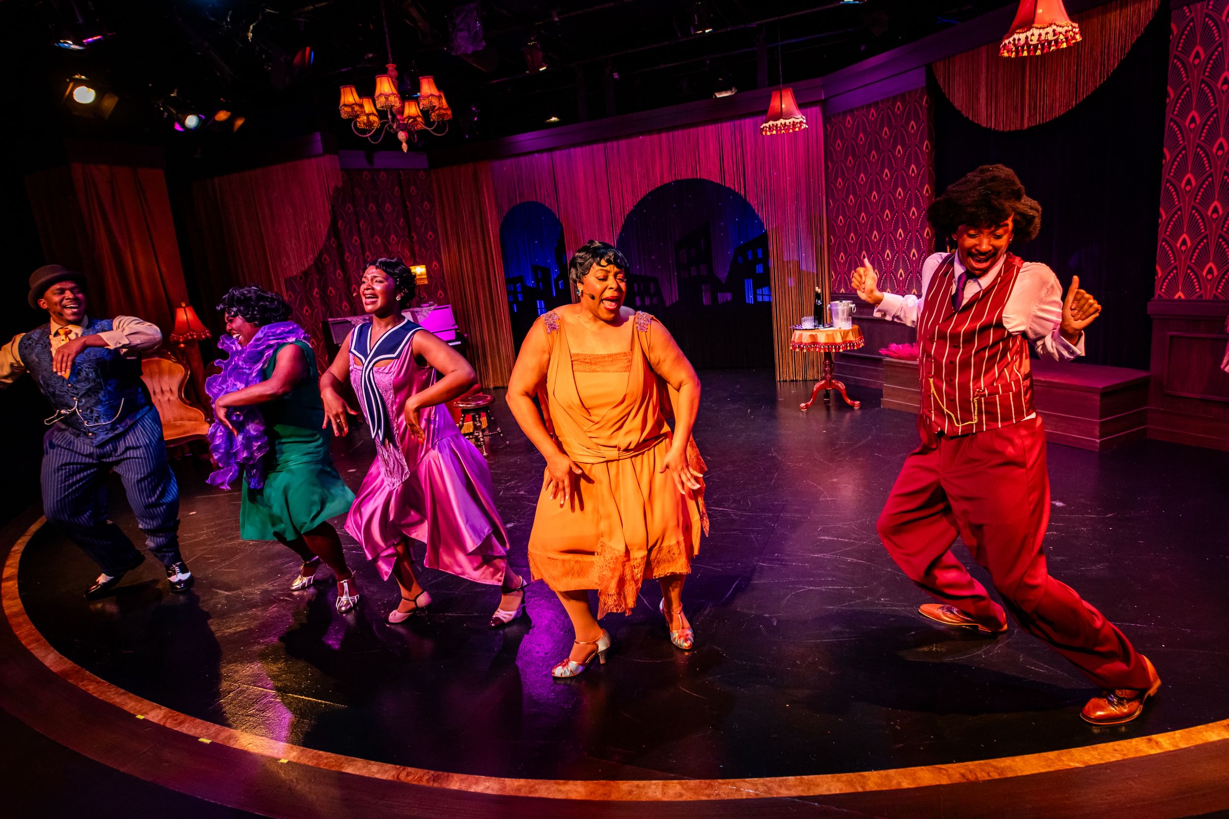 In colorful 1920s evening wear, the cast dances on the edge of semicircular stage decorated like a jazz club.
