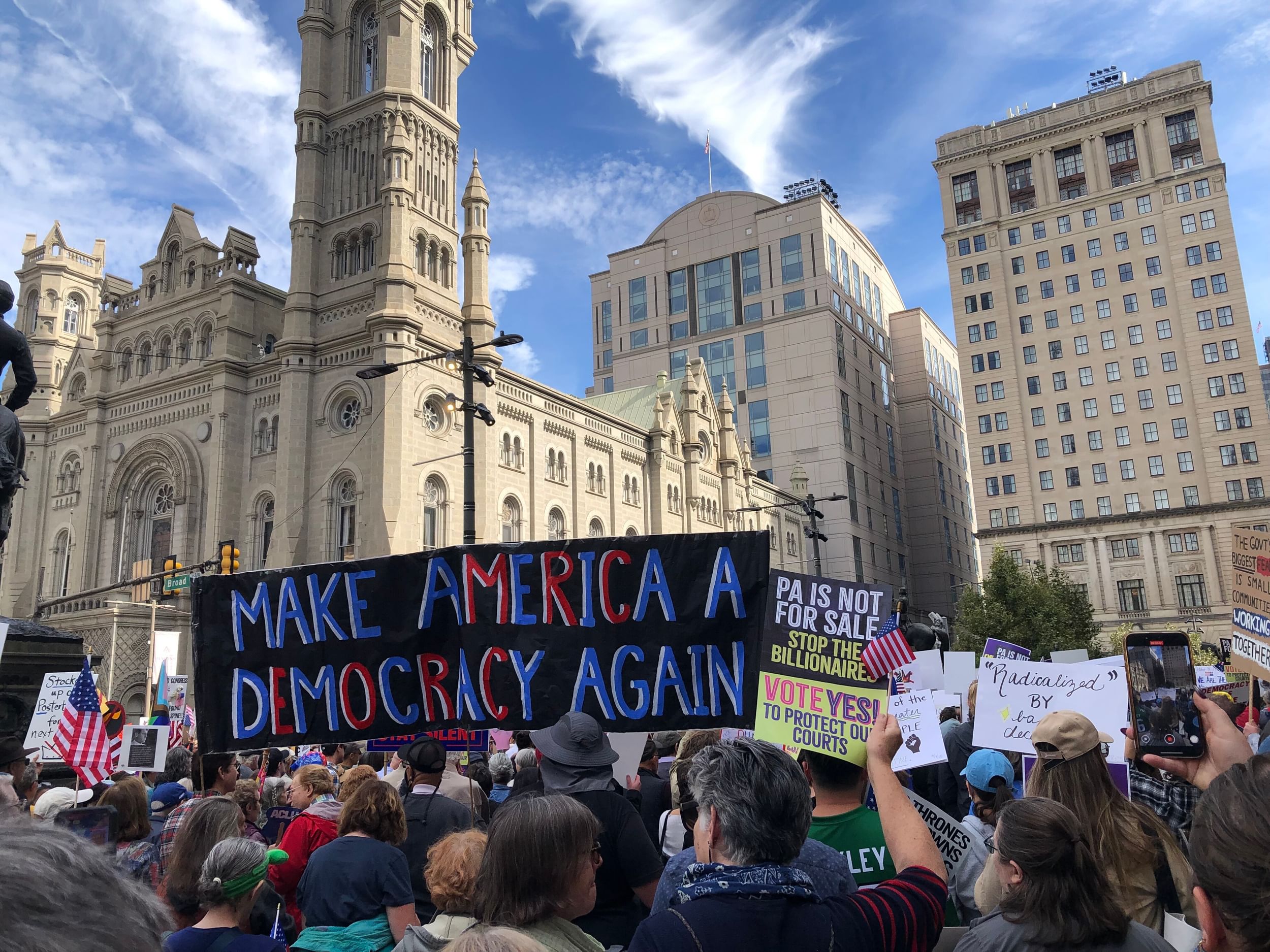View of a huge protest crowd on a sunny day, centered on a giant sign that says MAKE AMERICA A DEMOCRACY AGAIN