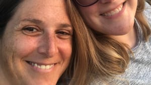 Smiling selfie of Alaina and Sara, two white women in their early 40s with light from the setting sun on their faces.