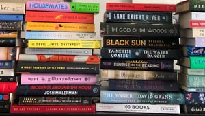 Close-up on four stacks of dozens of books in all genres.