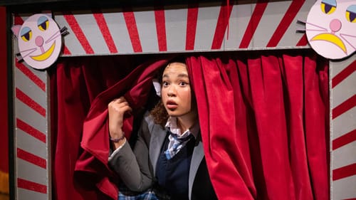 Solomon as Alice: a young Black woman peers apprehensively out of a red-and-white striped cardboard proscenium & red curtain