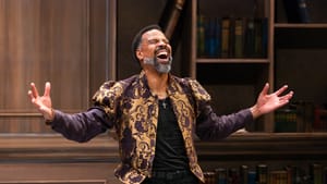 Brown, wearing black under a dramatic gold and purple Renaissance-style jacket, jubilantly spreads his arms.