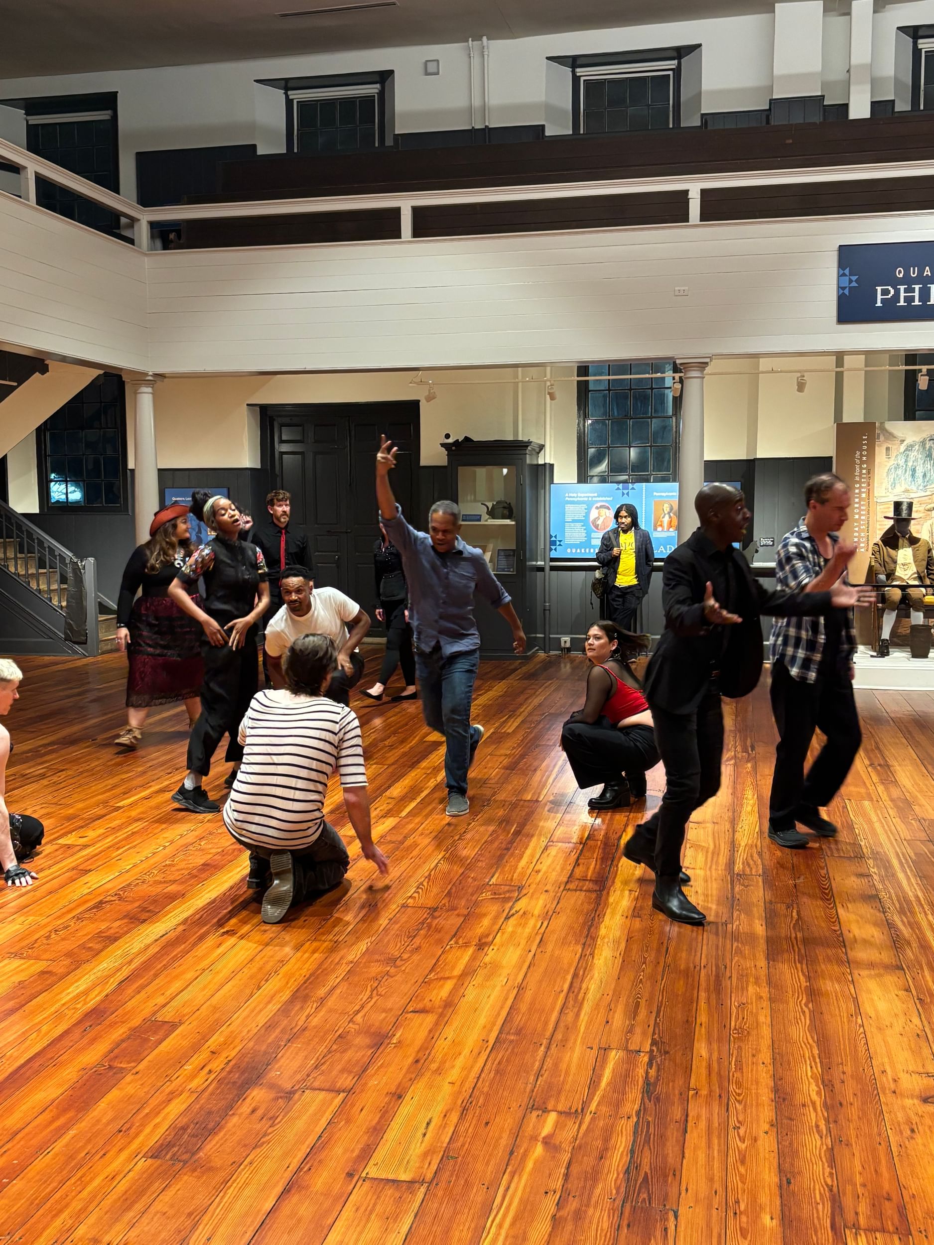 A diverse ensemble of 12 strikes a variety of poses together inside the two-story wooden meetinghouse.