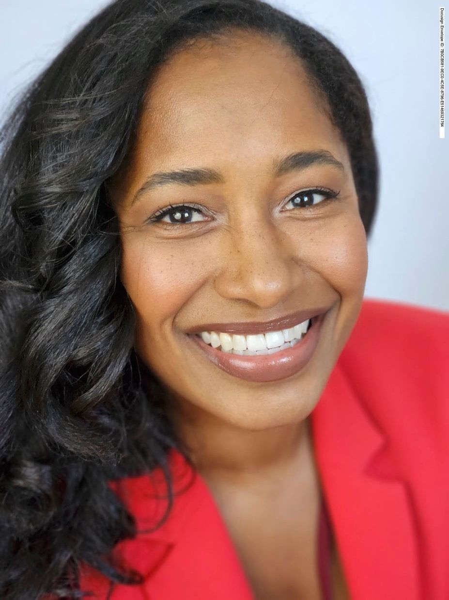 Closeup on Amina, a smiling Black woman with wavy hair, wearing a red blazer.