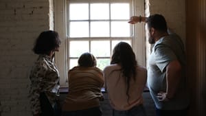 Four people in casual clothing look out a window in a white brick room. Bright light pours in from the window.