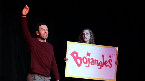 Behrend angrily holds a pen up; Snyder holds a sign reading “Bojangles” with a misplaced apostrophe which Behrend corrected