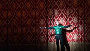 Costanzo, a white man wearing a sequined Eagles tee, spreads his arms excitedly in front of a luxe red & gold curtain.