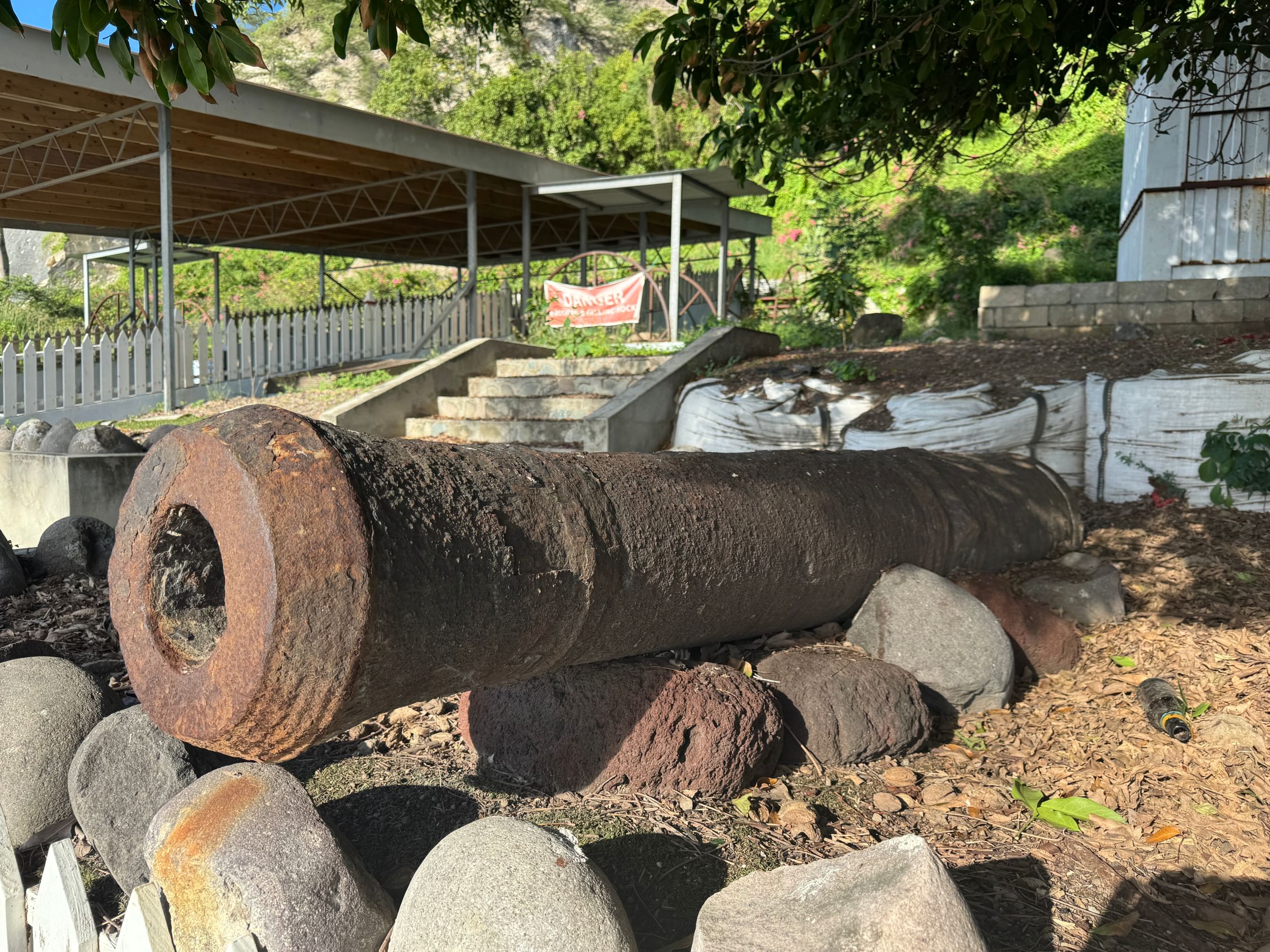 Outdoor view of a historic metal cannon with a thick, rusty metal barrel, resting on rocks on a sunny day.