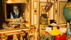 Phillips’s face appears at top left in the window of an ornate, mirrored shadowbox filled with dozens of vintage toys.