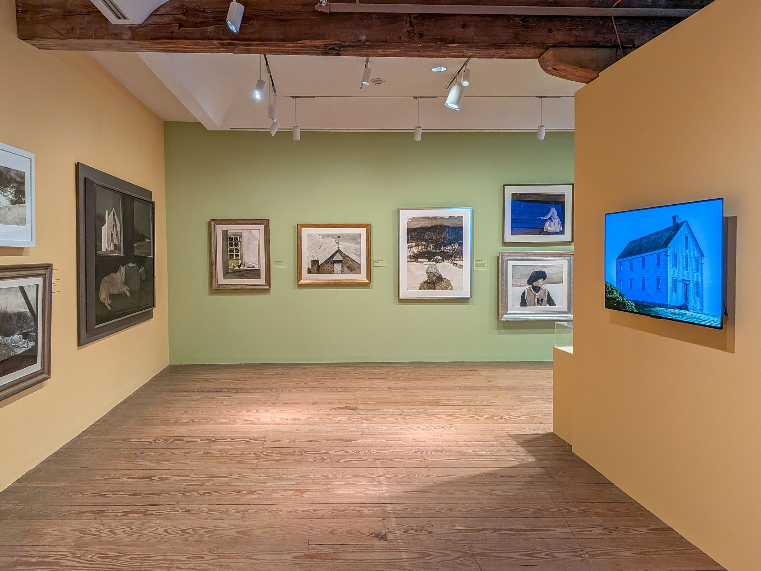 Gallery view of Wyeth paintings on muted yellow or green walls, above a natural-finish wood floor.