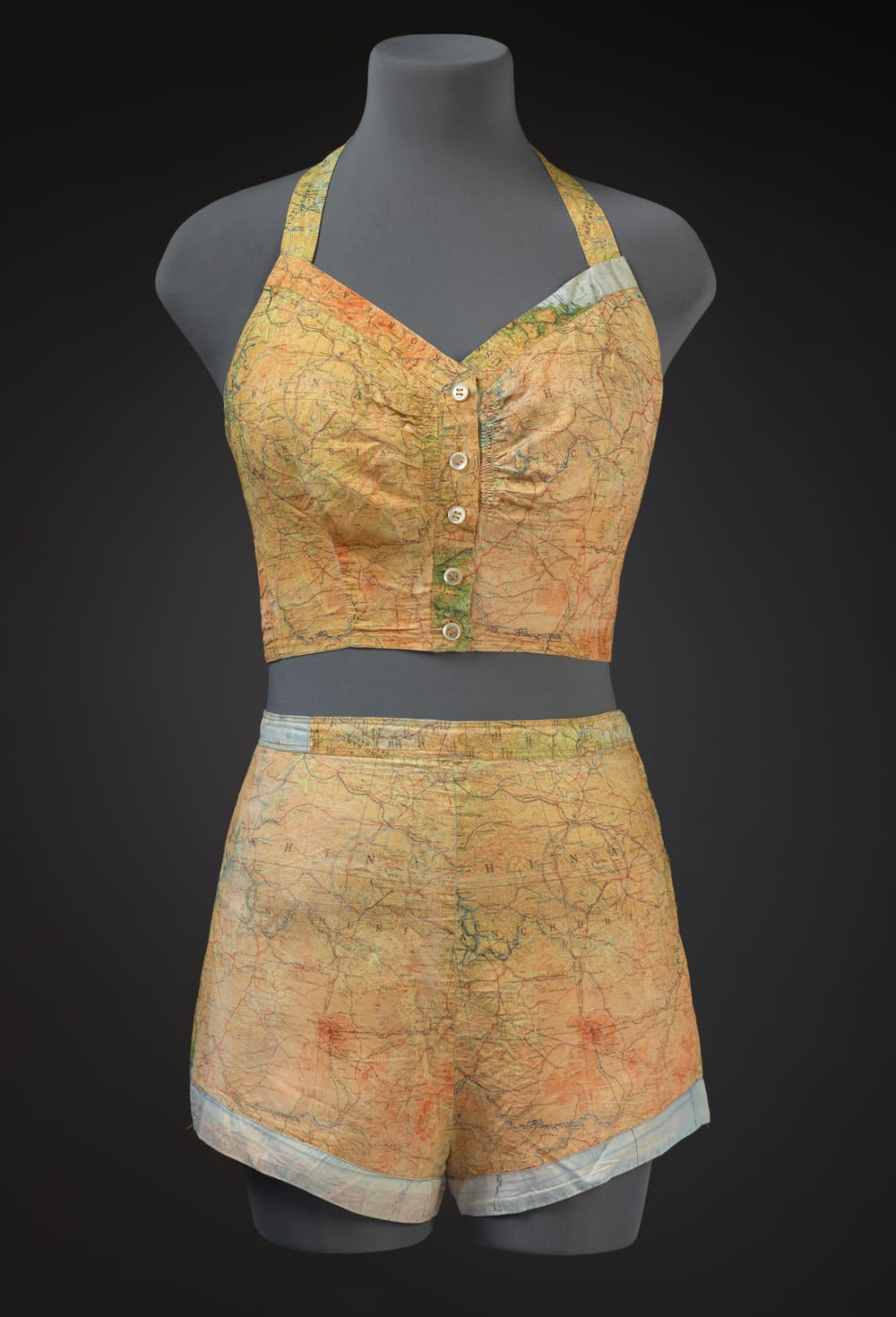 On a torso mannequin, a two-piece halter-and-shorts swimsuit made from a vintage WWII pilot’s map.