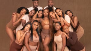 12 Black dancers in tan, brown & white lean tenderly in around another posing at center, long hair falling over one shoulder