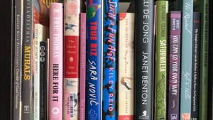 Close-up on about 16 colorful book spines on a black shelf, including R. Eric Thomas, Kiley Reid, Janet Benton, & Eric Smith