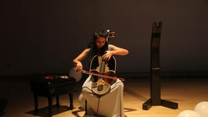 Khateri sits in a chair and looks down as she plays a Persian Qeychack, a bowed lute with a short fretless neck