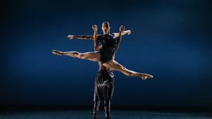 Two dancers on stage in pas de deux, one lifting the other dancer as they do a split in the air