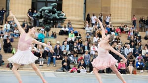 Two ballet dancers dance outdoors on a stage in front of the Philadelphia Museum of Art, an audience behind them