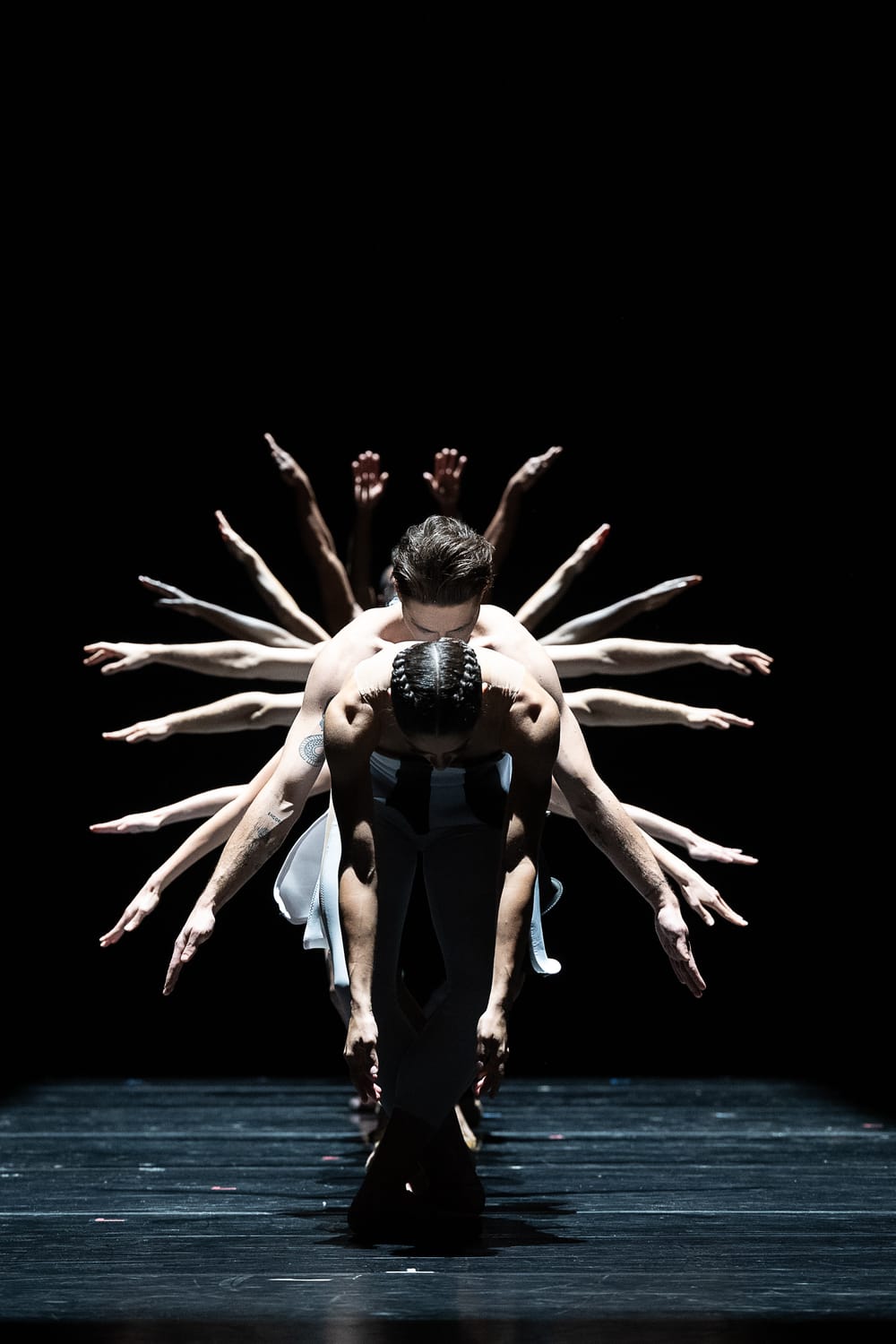 Several dancers stand behind Forcella, bowed at the waist, and all you can see are their arms spreading like a peacock tail