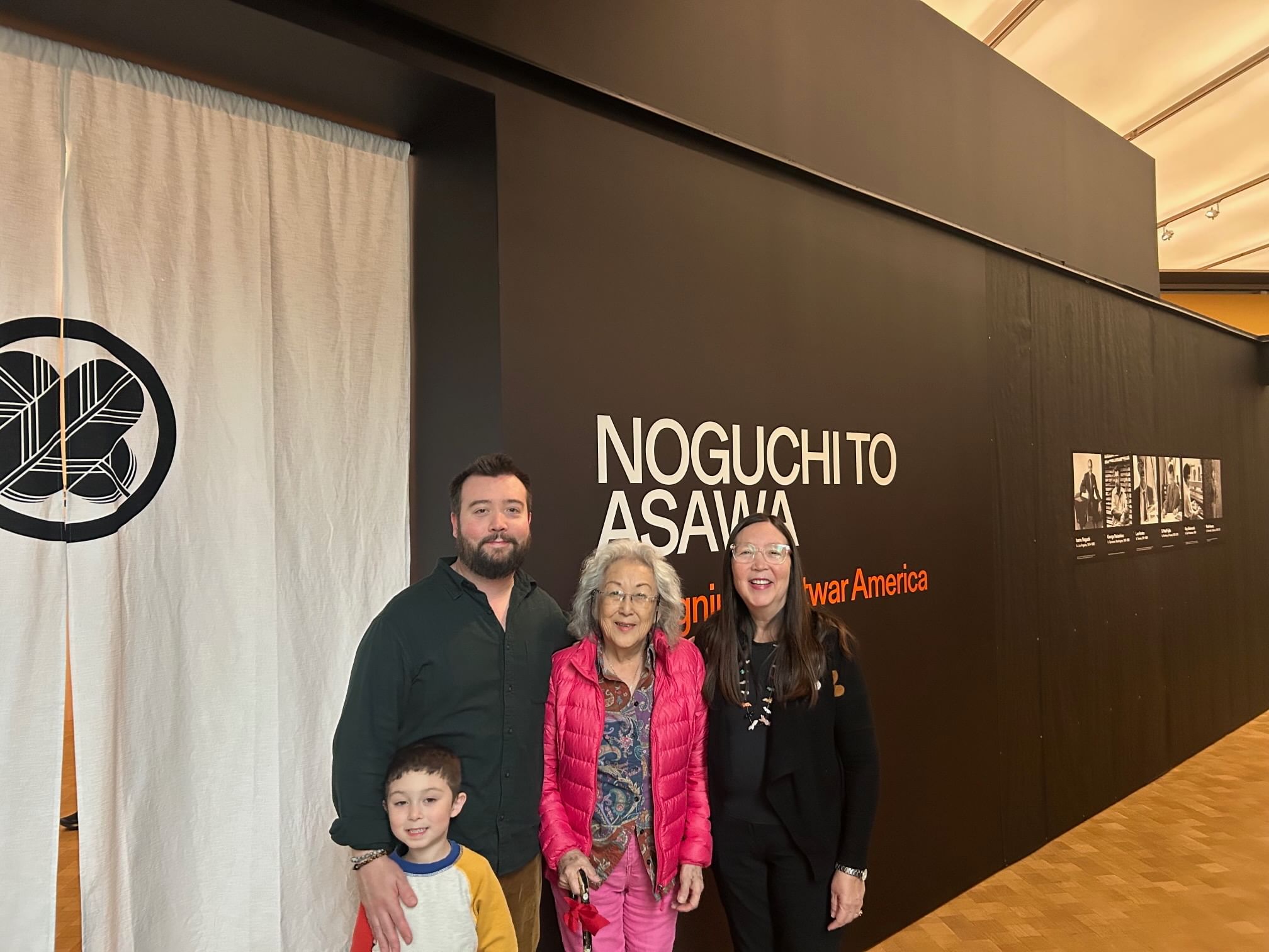 The family poses smiling together in front of the black entry wall of ‘Noguchi to Asawa: Designing Postwar America’