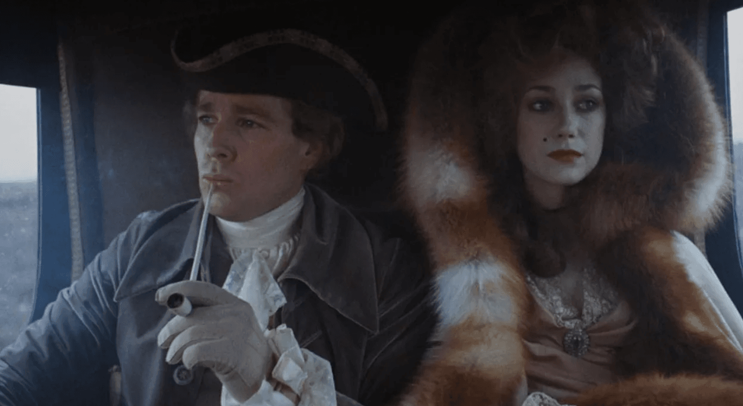 A man and woman in colonial dress, in what looks like a horse carriage