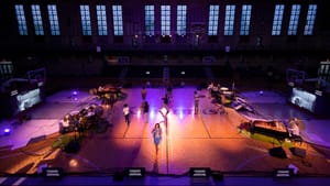 A wide shot revealing the whole Armory, lights on the court, dim everywhere else, all players on stage.