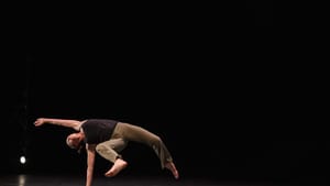 Bridge, horizontal to the black stage, strikes a flowing pose with her body suspended over one hand on the ground.