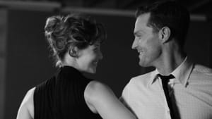 A black-and-white close-up film still of Caitriona Balfe and Jamie Dornan slowdancing and smiling at each other.