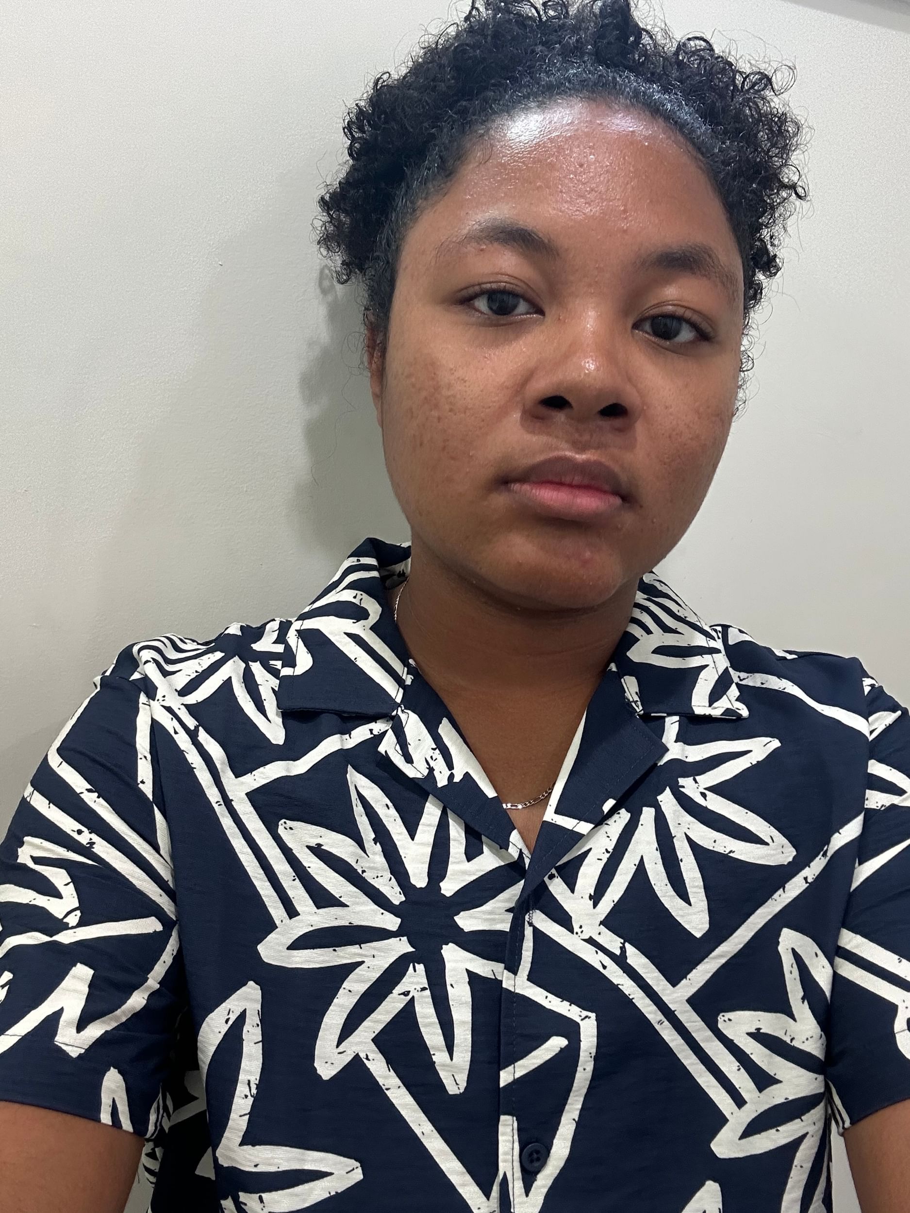 Kalli in a portrait-style photo wearing a black shirt with bold white lines against a plain white wall