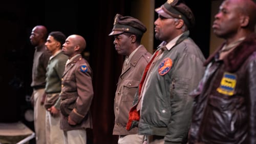 Six Black men playing 1940s airmen, seen in profile standing in a line in what looks like a barracks.