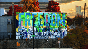 Book cover: title at top over a modern view of the city dominated by a brightly colored collage mural with the word FREEDOM.