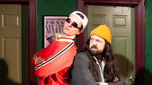 Two people pose back to back, arms crossed. One has sunglasses and backwards cap, the other looks over their shoulder
