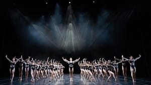 More than two dozen dancers fill the stage, dressed in black bandeaus, in unison of two different poses