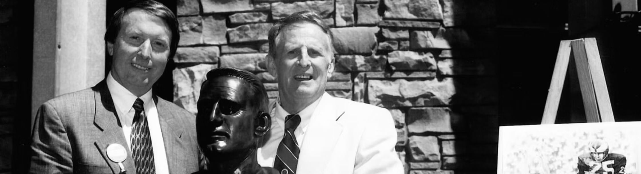 Vintage black & white photo of Ray Didinger and Tommy McDonald smiling next to a black statue of a man.