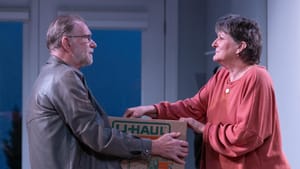 Scene from the play: the actors face each other with melancholy expressions, holding a cardboard U-Haul box between them.