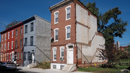 A three-story brick rowhome stands alone because of a demo. Outlines of the destroyed rooms & stairs are visible on its side