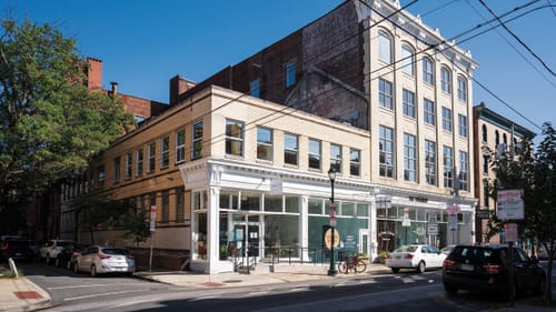 The ghost of a pointed roof is visible on the brick side of a 4-story building next to a modern 2-story one.