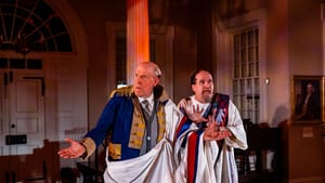 Schmitz, as Washington with a toga over his military garb, looks confused next to McCann in a toga accented with the US flag