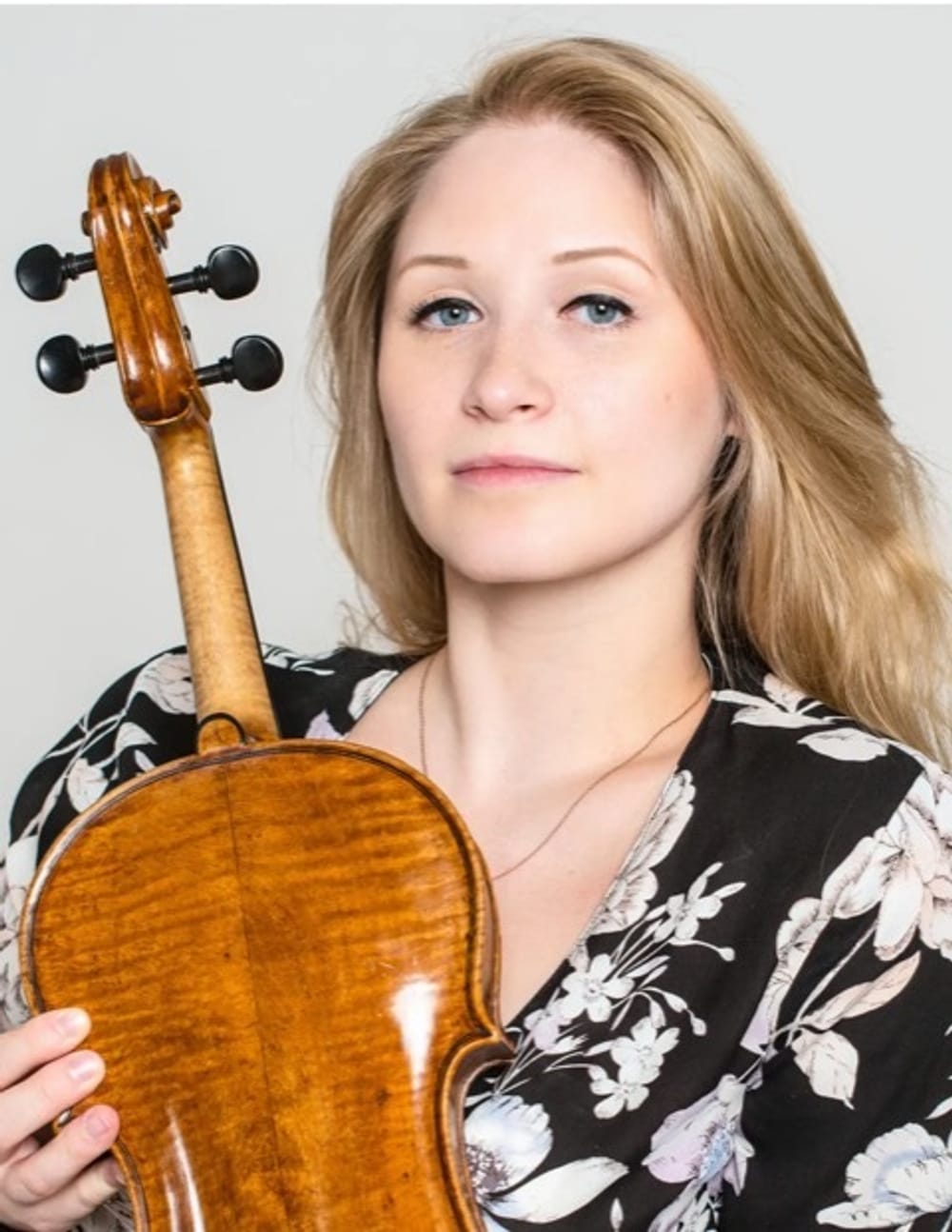 Smith has blonde hair and a black floral print top and poses for a portrait-style photo with a viola