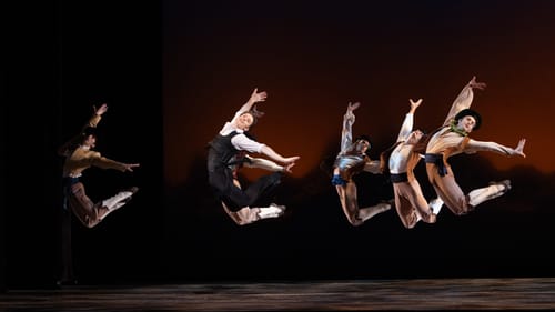 Six male dancers leap together in the same curving pose, right arm reaching up and other limbs extended to the right.