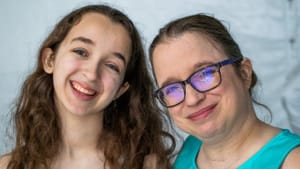 Carrie, a white woman in her 40s with glasses, stands smiling with her teen daughter. Both wear turquoise dresses.