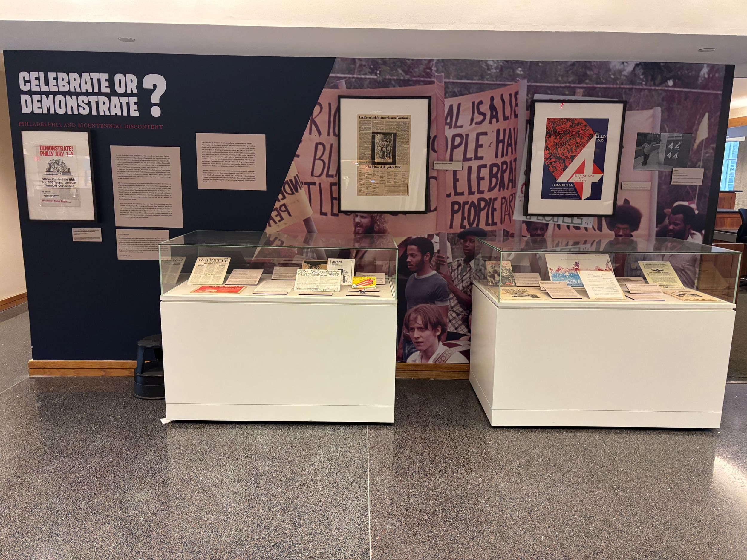 Two vitrines full of documents from the era in front of a wall with more framed documents and a large image from 1976 protest