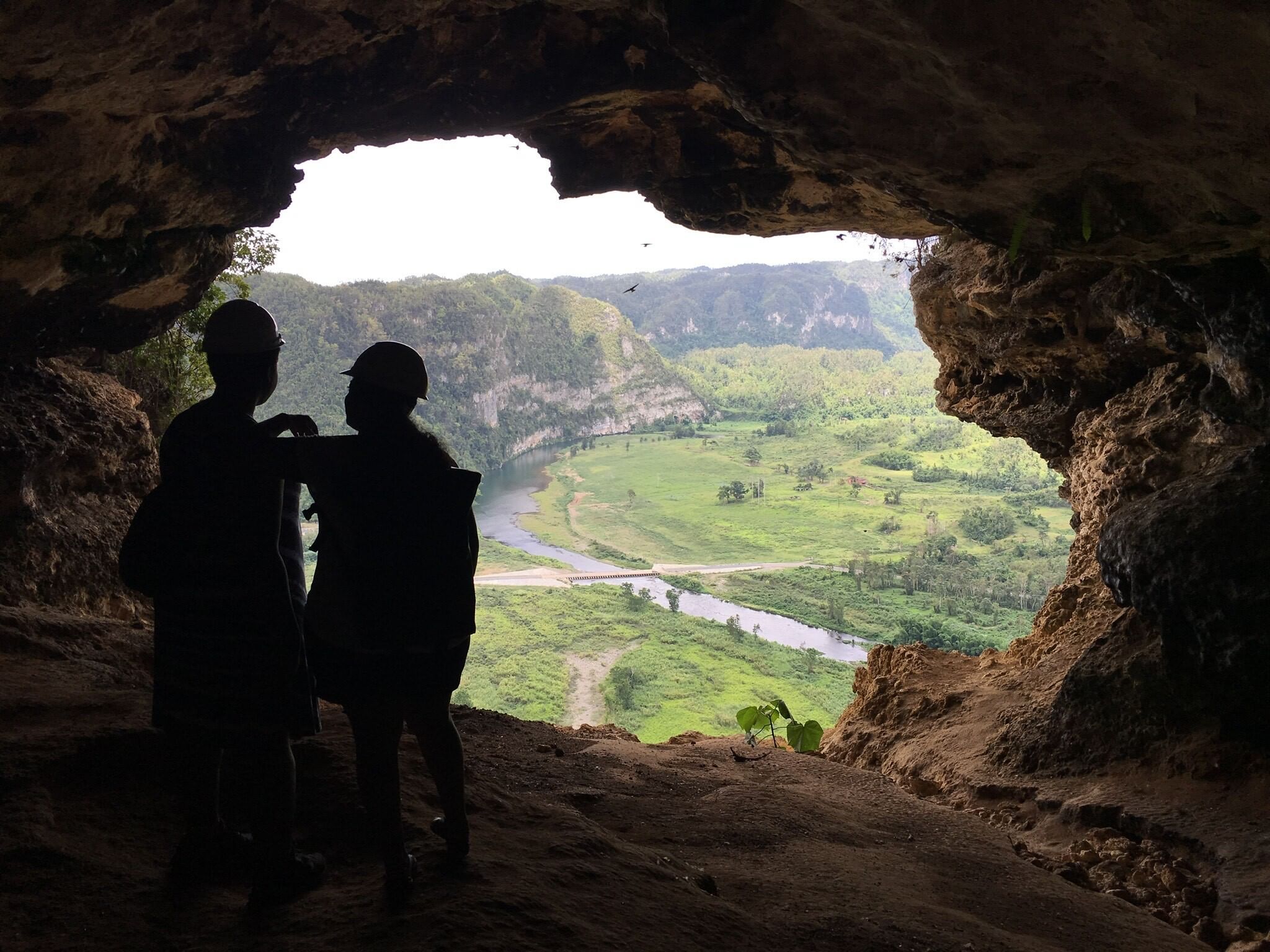 A photo from inside a scenic mountain cave in Puerto Rico, showing two people in silhouette in front of a grand tropical view